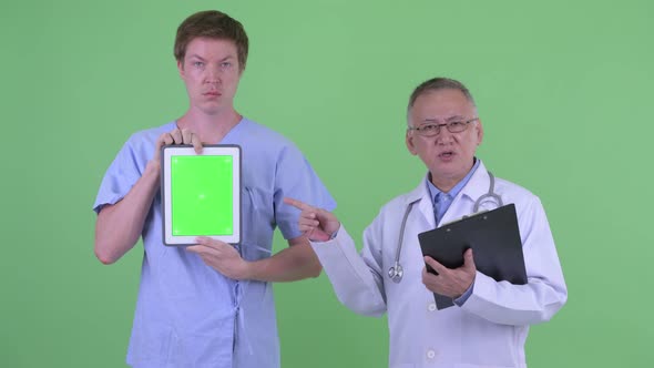 Mature Japanese Man Doctor with Young Man Patient Showing Digital Tablet and Explaining Something