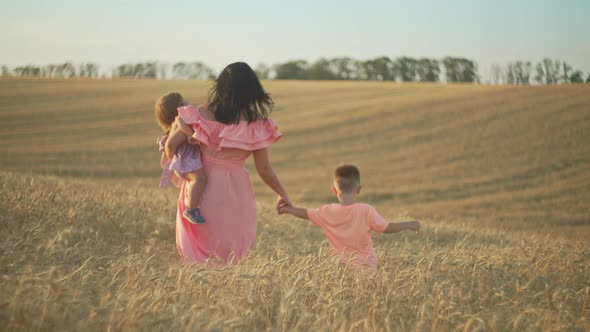 A Mother and Her Children are Walking Along a Wheat Field