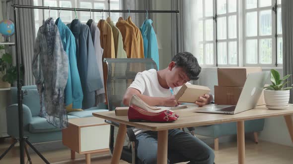 Asian Man Online Seller Looking At The Package And Writing In The Notebook While Selling Online