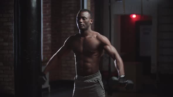 A Black Handsome Man Pumping His Hands Muscles with Dumbbells in the Gym