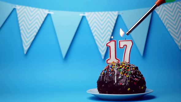 chocolate birthday cake with a burning candle number seventeen, 17 on a blue background. Copy space.