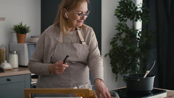 Caucasian senior woman cooking and chatting via earphones. Shot with RED helium camera in 8K