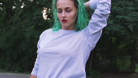 Young Stylish Funky Girl with Green Hair Riding Roller Skates and Dancing in Park Slow Motion