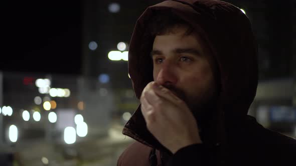 A Young Man Stands in the Cold in the Evening Outside and Warms His Hands with His Breath.