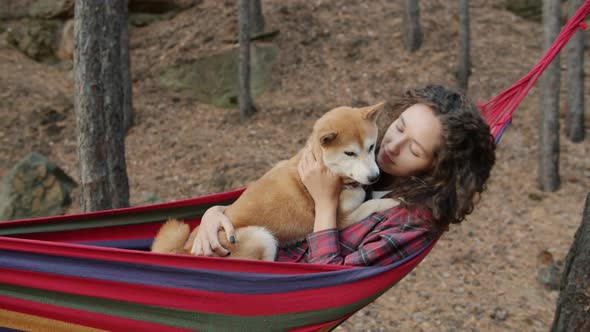 Cute Girl Relaxing in Hammock with Shiba Inu Dog Spending Leisure Time in Autumn Forest