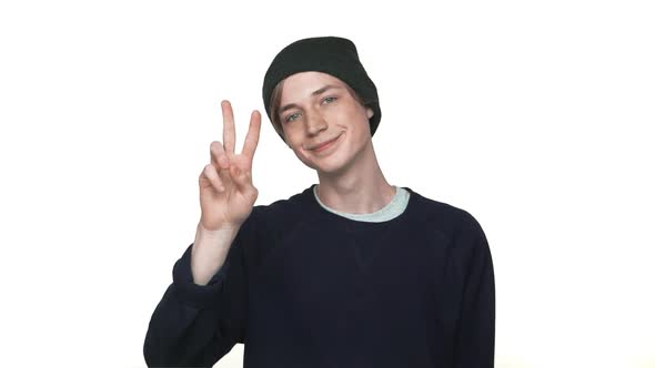 Portrait of Smiling Caucasian Thin Youngster Wearing Hat Showing Two Fingers Victory Sign Gesturing