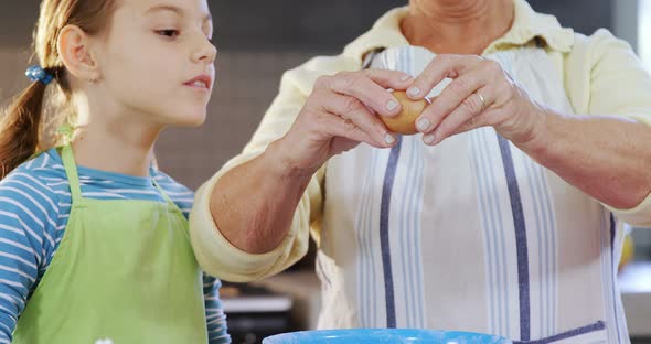 Grandmother breaking an egg in bowl and little girl watching 