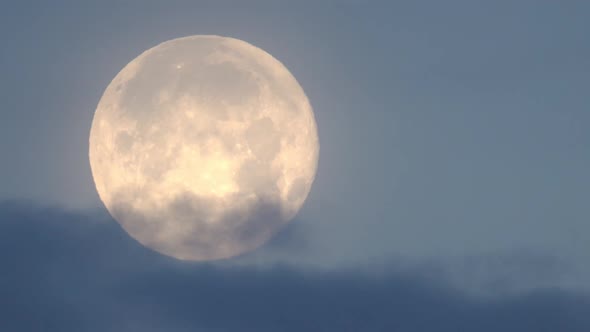 Full Moon moving through the sky behind clouds