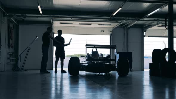 Two Professionals are Looking at the Racing Car in the Workshop