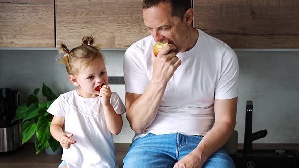 Cute Little Girl and Her Handsome Dad are Eating Fruit in Modern Kitchen