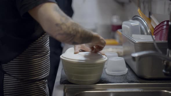 Tattooed Male Chef Uses Salad Sling Machine in Restaurant Kitchen