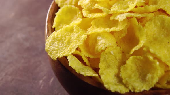 A full rustic wooden bowl of cornflakes on a wood surface. Macro