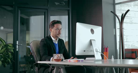 Businessman in Glasses Sits at Computer in Office