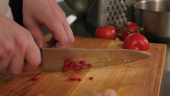 Closeup of a Chef Slicing Hot Chili Peppers on a Chopping Board in a Kitchen