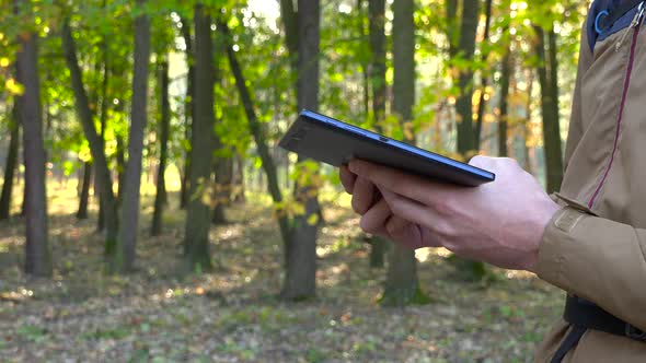 A Backpacker Looks at a Tablet in a Forest - Closeup From the Side