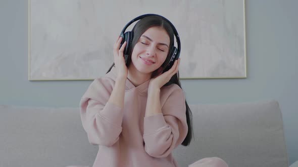 Young Caucasian woman listening music with headphones while sitting on sofa.