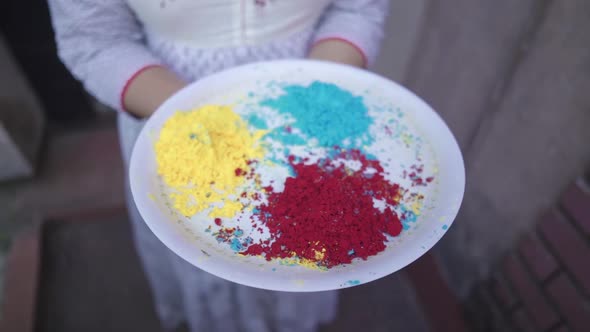 Unrecognizable girl holds tray of colored powders on Holi outdoor, slow motion