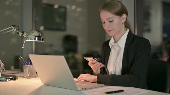 Young Businesswoman Using Cellphone on Office Desk at Night
