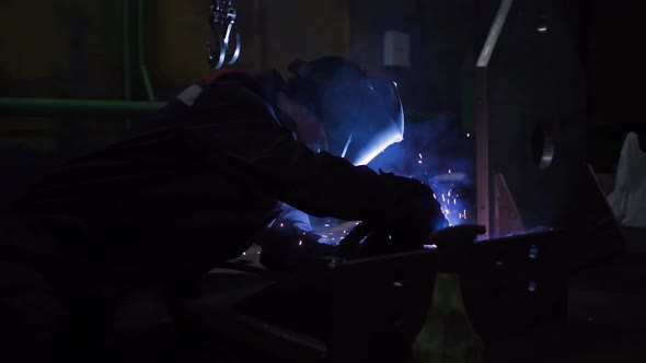 Professional worker in mask welds parts at the factory