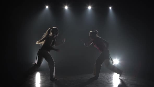 Women Practicing Capoeira in Darkness Against Spotlight in Studio