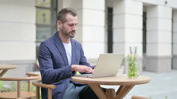 Man Working on Laptop While Sitting in Outdoor Cafe