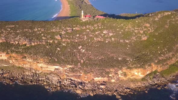 Aerial revealing shot of Barrenjoey Head Lighthouse on the top of headland sandstone rock in sunrise