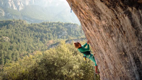 Strong and Powerful Woman Rock Climber Climbs Hard Tough Rock Route on Overhanging Cliff on