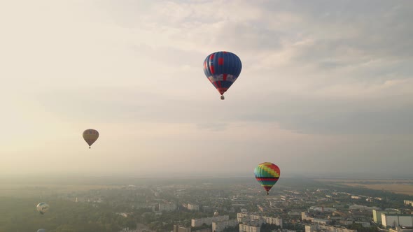 Colorful Hot Air Balloons Flying Over Buildings in Small European City at Summer Sunset, Aerial View