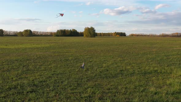 The Boy Runs with a Kite on a Green Field