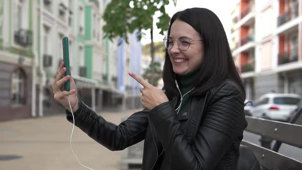 Happy young girl making a video call, smiling, talking on the background of a city street.