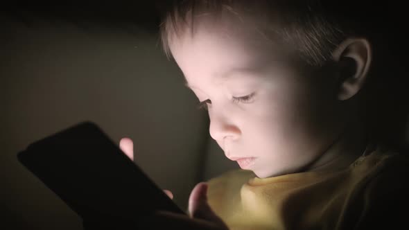 Little Boy, Sitting in a Dark, Playing with Smartphone
