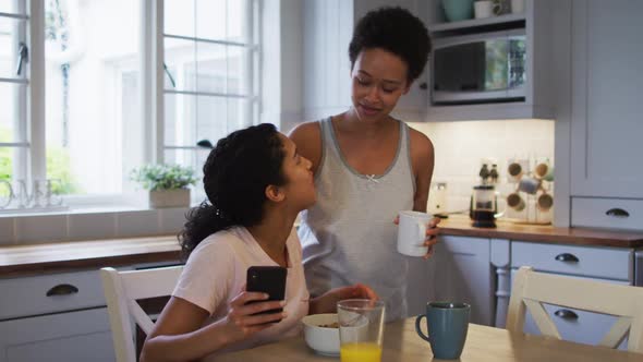 Mixed race lesbian couple hugging and drinking coffee in kitchen