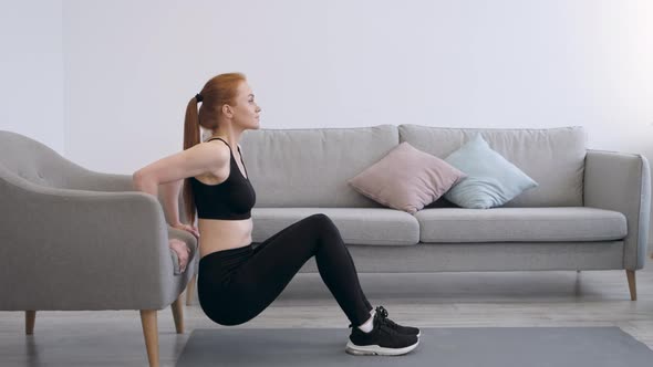 Fitness Woman Doing Squats Exercising Near ArmChair At Home