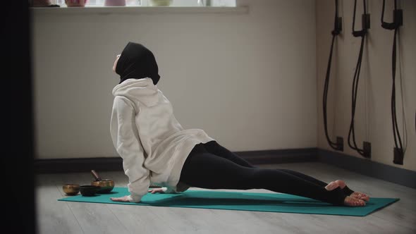 Yoga Indoors  Young Woman in Hijab Warming Up Her Body on Yoga Mat