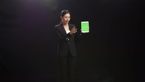 Asian Speaker Woman Holding And Pointing Green Screen Tablet While Speaking In The Black Studio