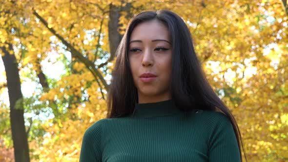 A Young Asian Woman Talks to The Camera in A Park