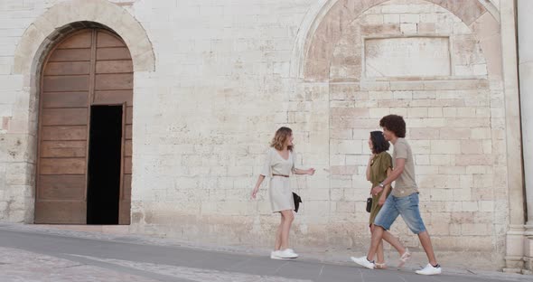 Three Happy Tourist People Friends Walking, Smiling and Having Fun Near a Brick Wall in Rural Town