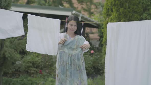 Attractive Mature Woman with Long Hair Hanging Her Clothes on a Clothesline Outdoors