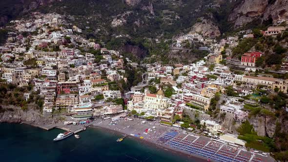 Positano town in the Amalfi coast of Italy with boat and crowded beach umbrellas, Aerial pan left ap