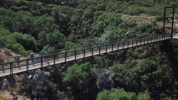 Drone Shot following an active man running on an outdoor hanging suspension bridge above Bear Canyon