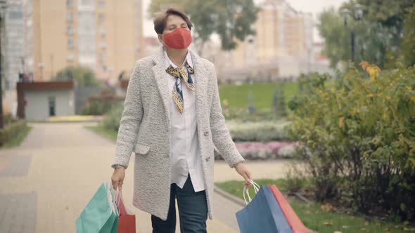 Confident Senior Caucasian Woman in Covid Face Mask Walking with Shopping Bags in City