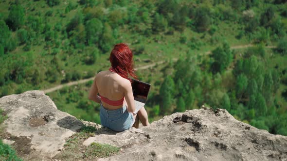 Girl Blogger Traveler is Typing Text on Laptop While Sitting on Top Mountain