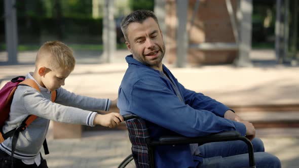 Side View of the Son Went for a Walk with His Disabled Father and Pushes His Wheelchair and Father