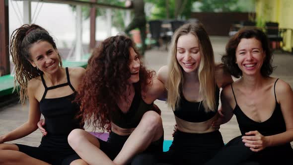 Smiling Girls in Sportwear Sit in an Embrace on the Floor After Practicing Yoga