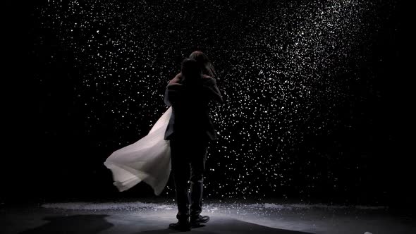 Cute Couple in Love on the Background of Falling Snow. A Man Circles His Beloved Woman on a Black