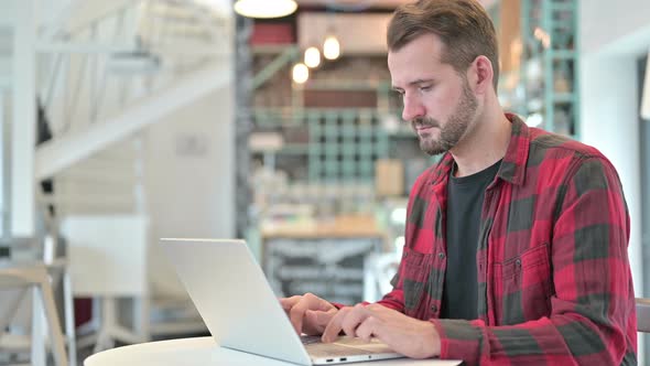 Serious Young Man with Laptop Looking at Camera in Cafe 