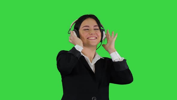 Young Business Woman Listening To Music in Headphones and Dancing on a Green Screen, Chroma Key.