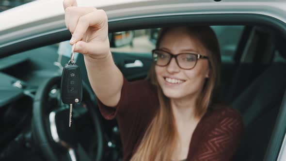 Young Caucasian Happy Woman Sitting on the Driver Seat in the Car and Holding Keys