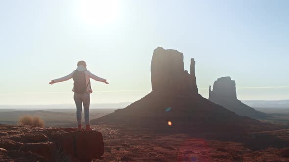 Woman Traveller with Arms Raised on Top of Mountain Looking at Monument Valley