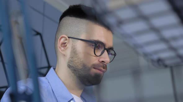 Concentrated young man freelancer in eyeglasses looking at laptop screen, working remotely at home.